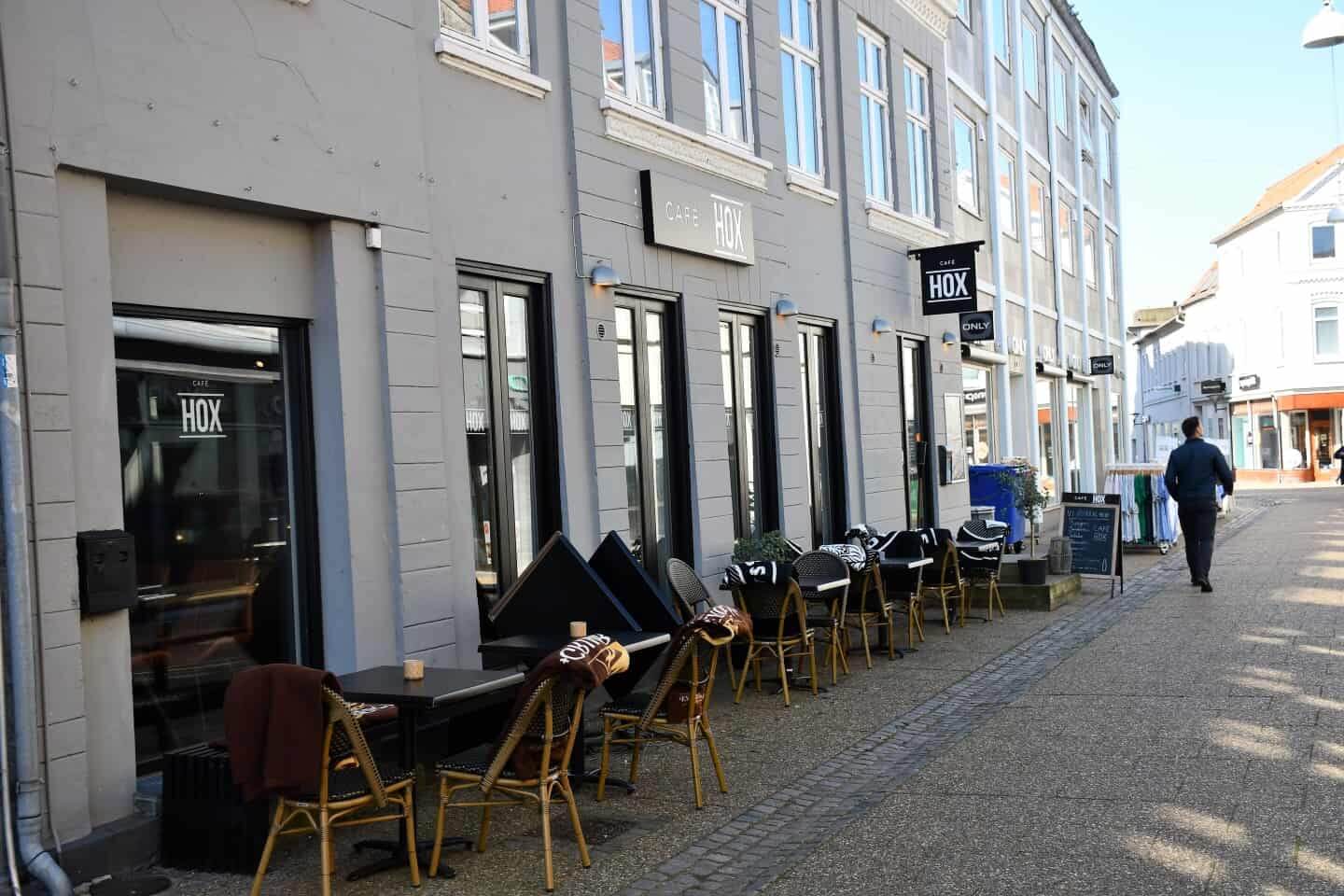 Udendørs servering foran Café HOX på en stille gågade med borde og stole langs facaden