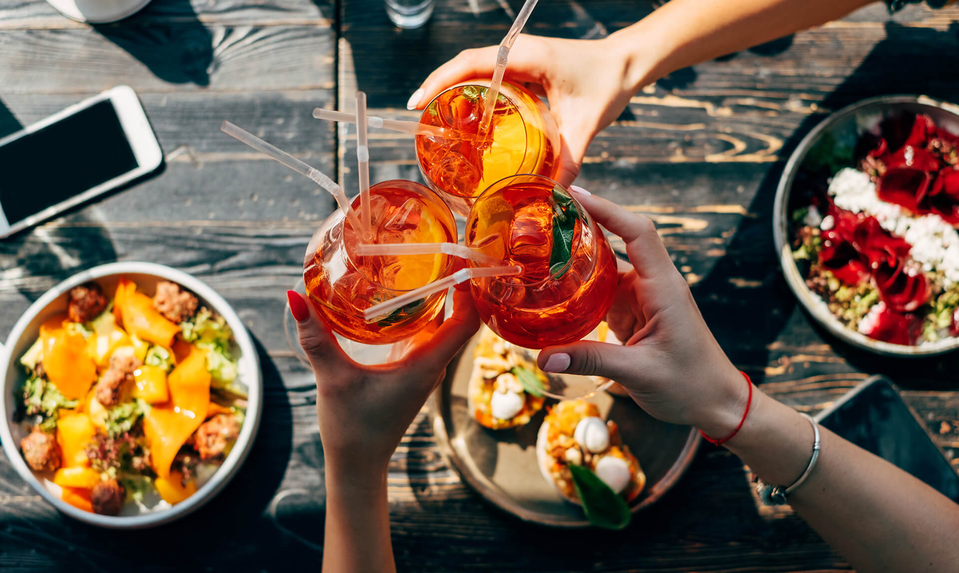 Flere personer skåler med drinks over et bord med småretter