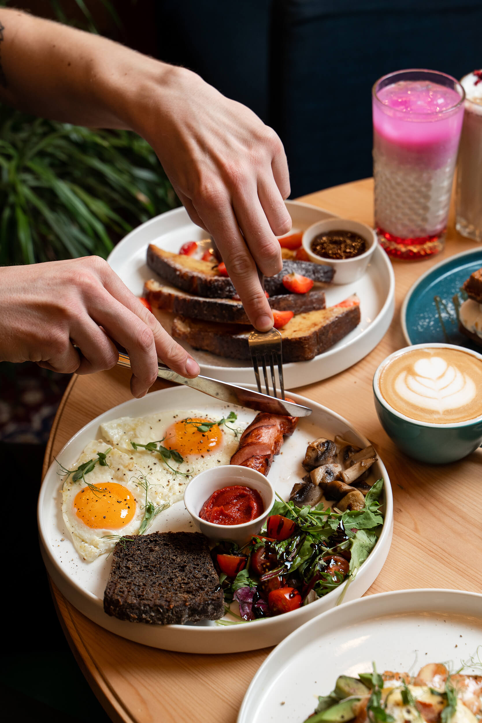 Person skærer i en brunchanretning med æg og tilbehør ved et cafébord