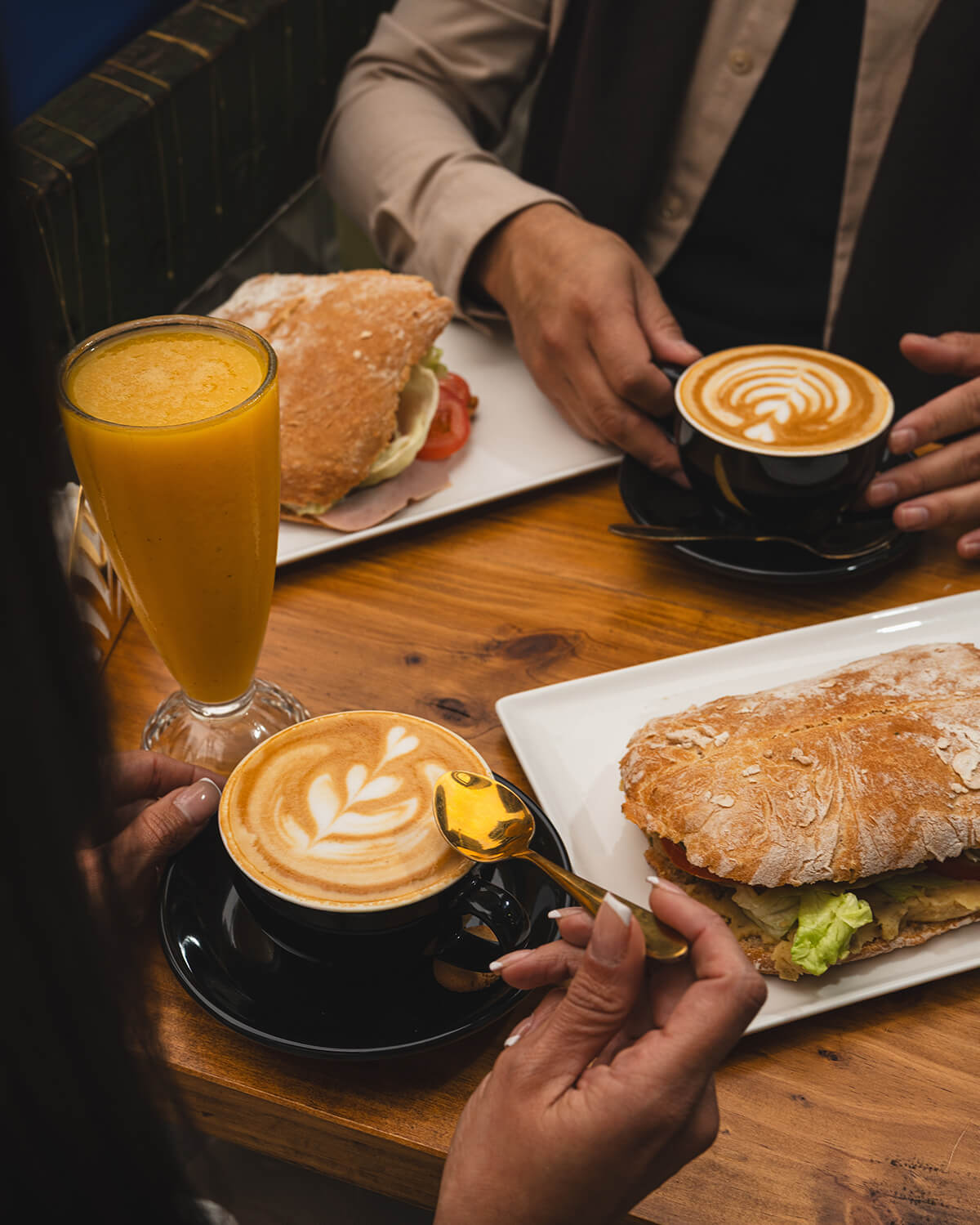 To personer nyder kaffe og sandwich ved et cafébord