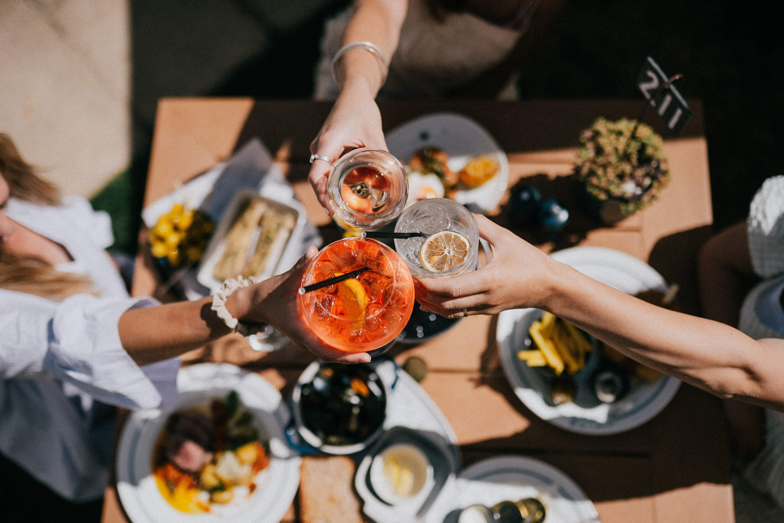 Flere personer skåler med drinks over et dækket bord